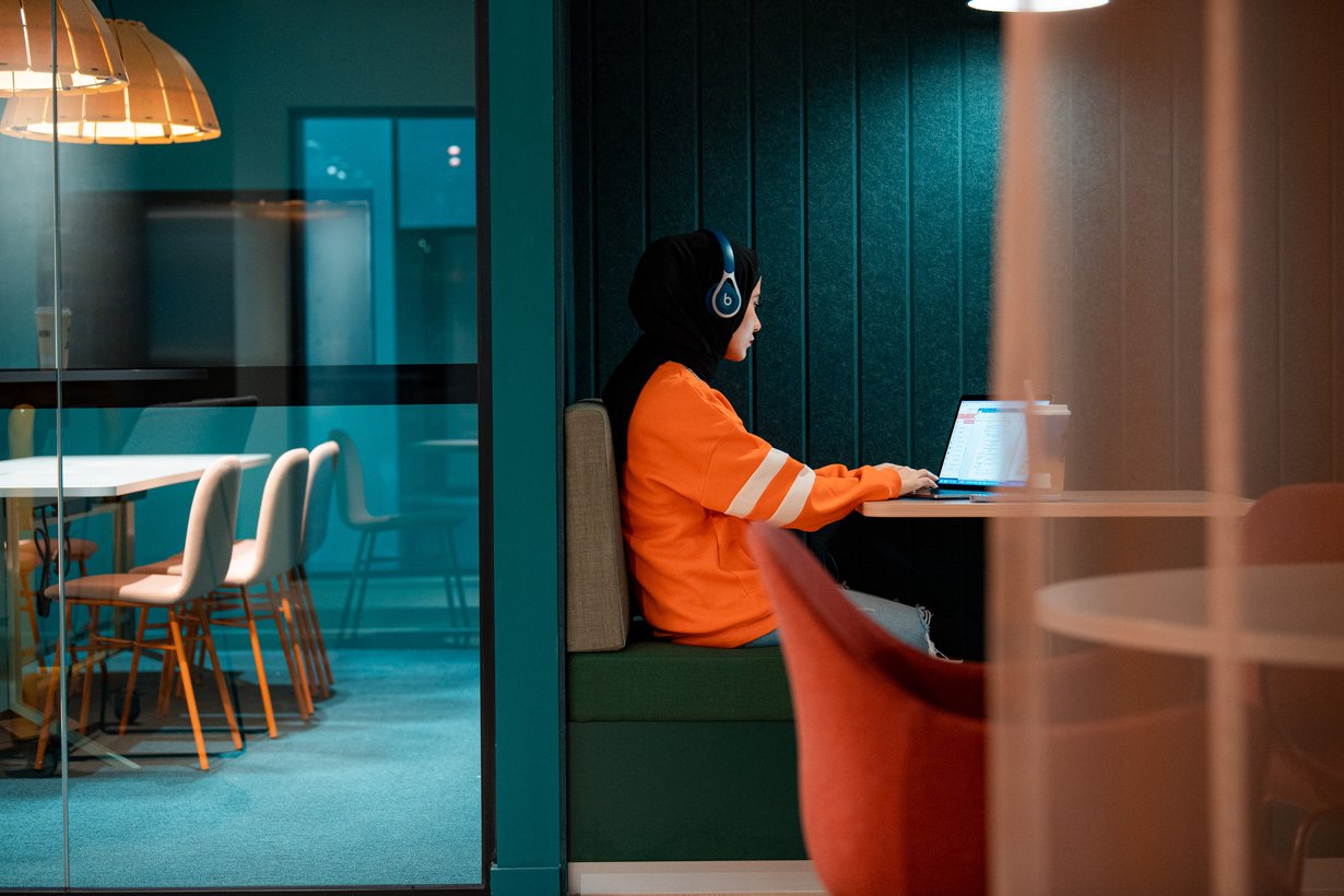 Resident sitting with headphones and laptop in common area at Scape Lincoln College student accommodation.