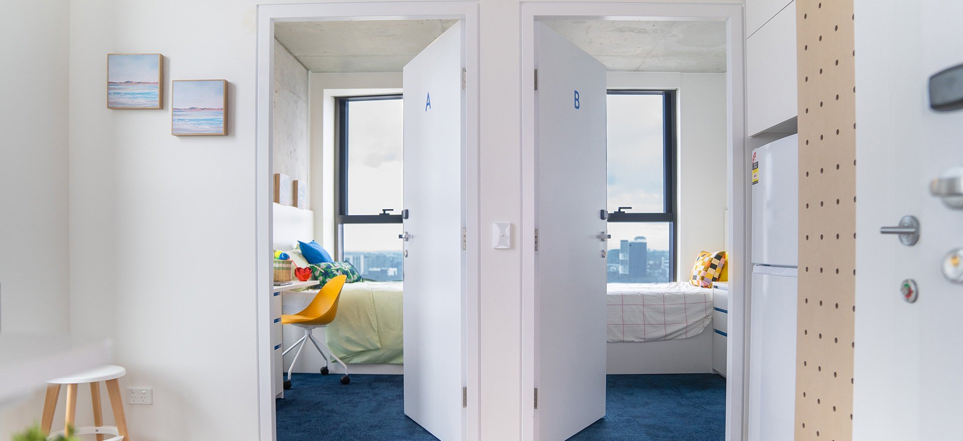 Two identical, minimalist bedrooms are visible through open doorways in a light blue-toned apartment.
